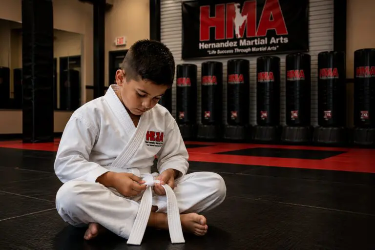 Young karate student tying his belt at Hernandez Martial Arts while learning perseverance and confidence
